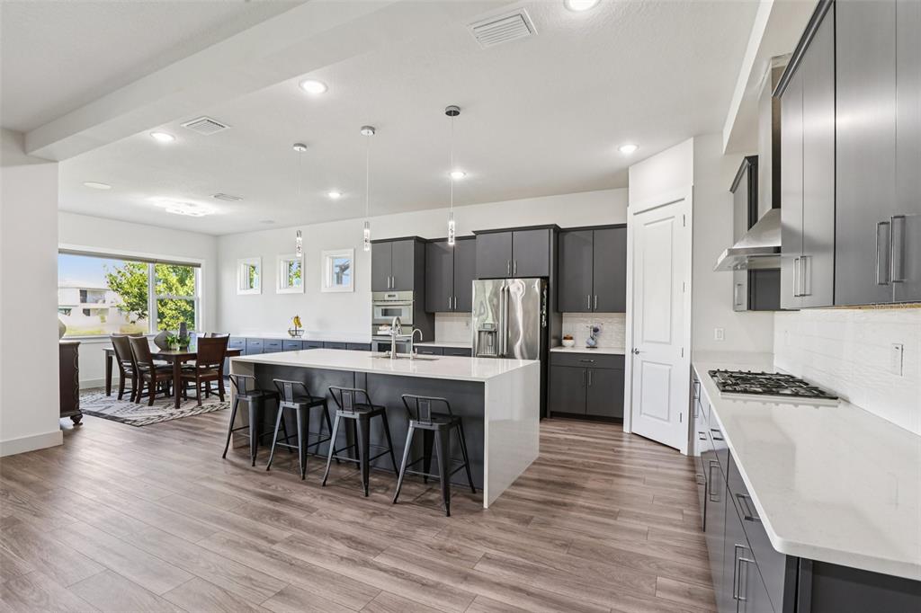 8743 Sanders Tree Loop Wesley Chapel, FL 33545 - Photo 7 of 41 a kitchen with stainless steel appliances kitchen island granite countertop a stove refrigerator and a dining table with wooden floor
