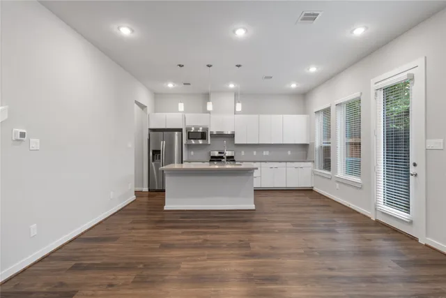 a view of kitchen with kitchen island stainless steel appliances wooden cabinets and wooden floor