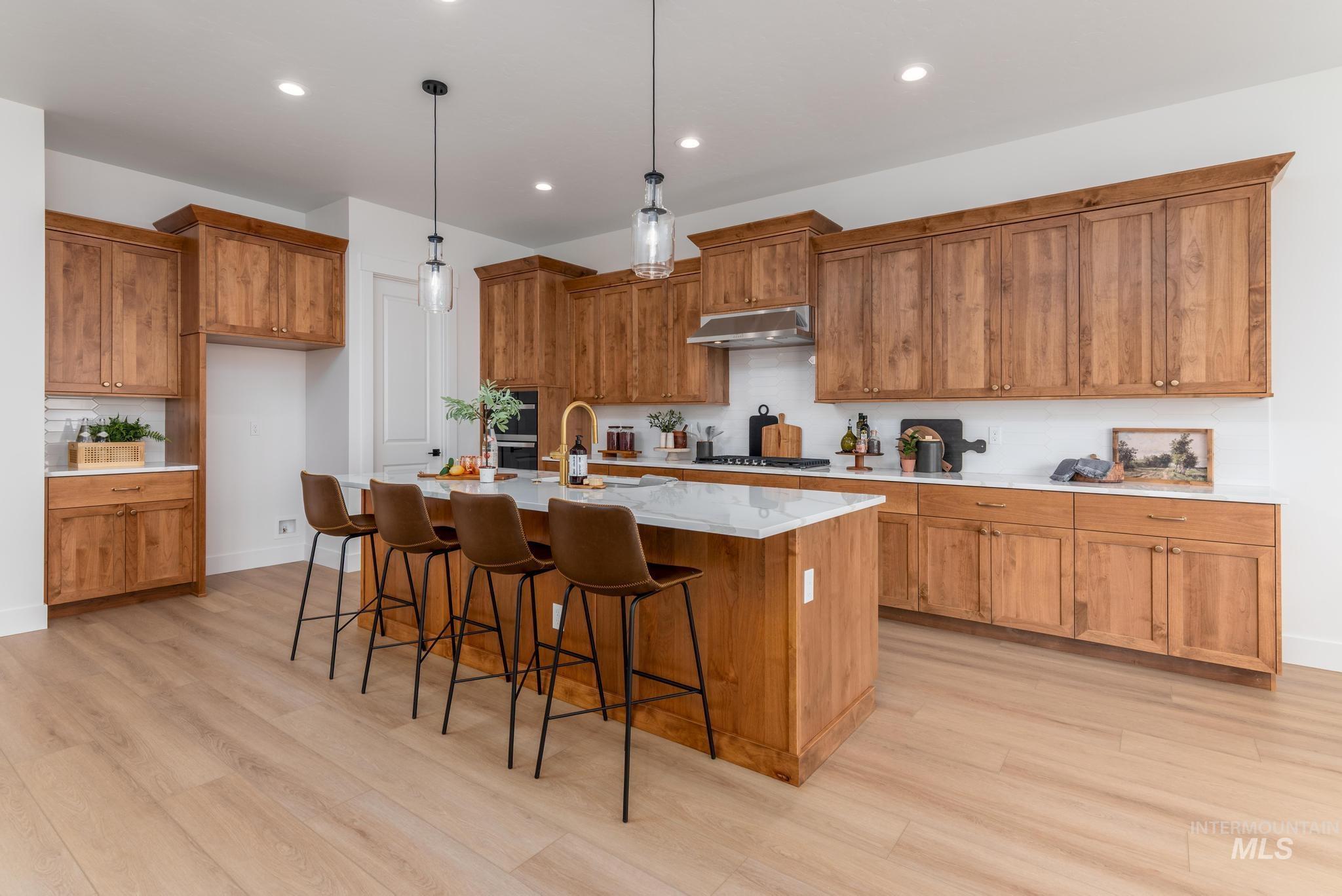 8569 South Silver Smog Way Meridian, ID 83642 - Photo 6 of 14 Kitchen with wood finish cabinets, a kitchen breakfast bar, light stone counters, an island with sink, and pendant lighting