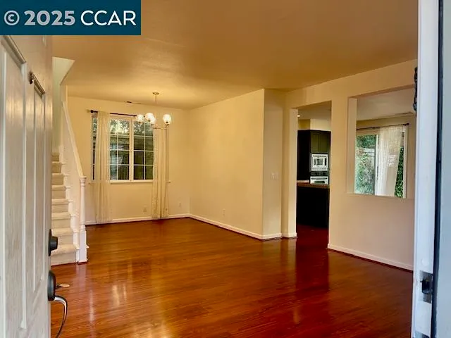a view of an empty room with wooden floor and a kitchen