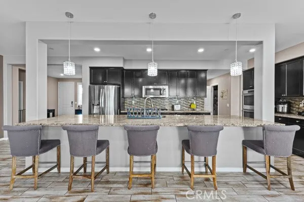 a kitchen with stainless steel appliances kitchen island granite countertop a dining table chairs and a refrigerator