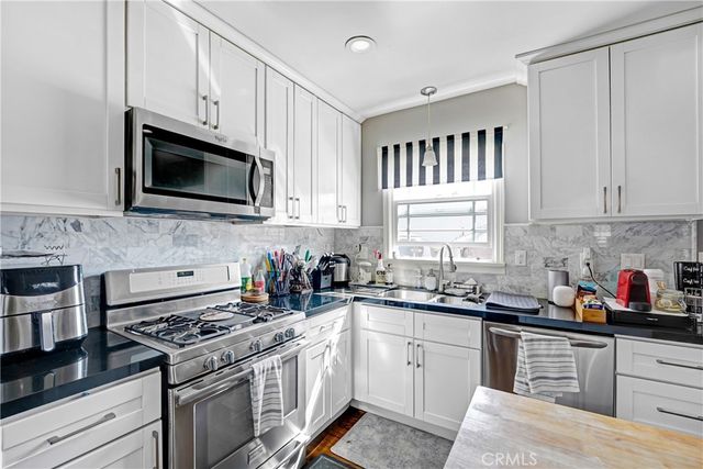 a kitchen with stainless steel appliances granite countertop white cabinets a sink dishwasher a stove and a microwave oven with cabinets