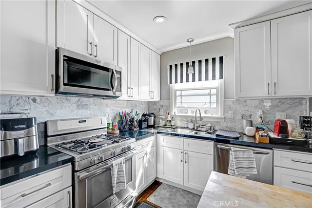 a kitchen with stainless steel appliances granite countertop white cabinets a sink dishwasher a stove and a microwave oven with cabinets