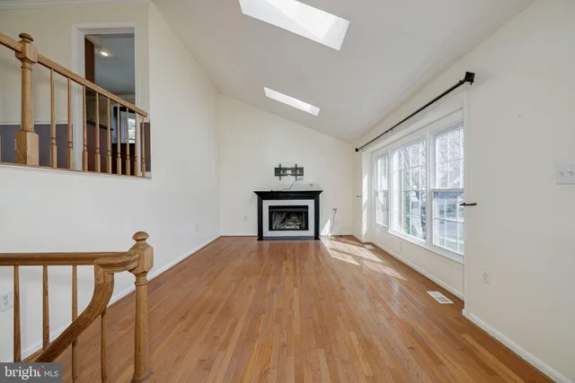 a view of an empty room with wooden floor fireplace and a window