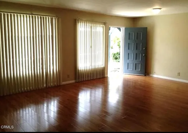 an empty room with wooden floor and windows with curtains