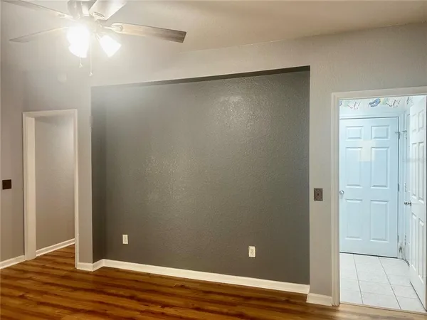 an empty room with wooden floor and fan in hallway