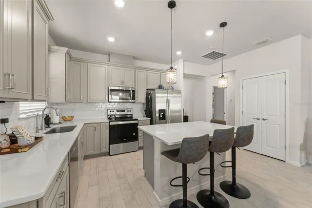 a kitchen with stainless steel appliances kitchen island granite countertop a dining table chairs refrigerator and sink