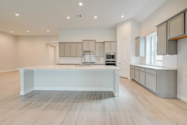 a large white kitchen with kitchen island a sink stainless steel appliances and cabinets