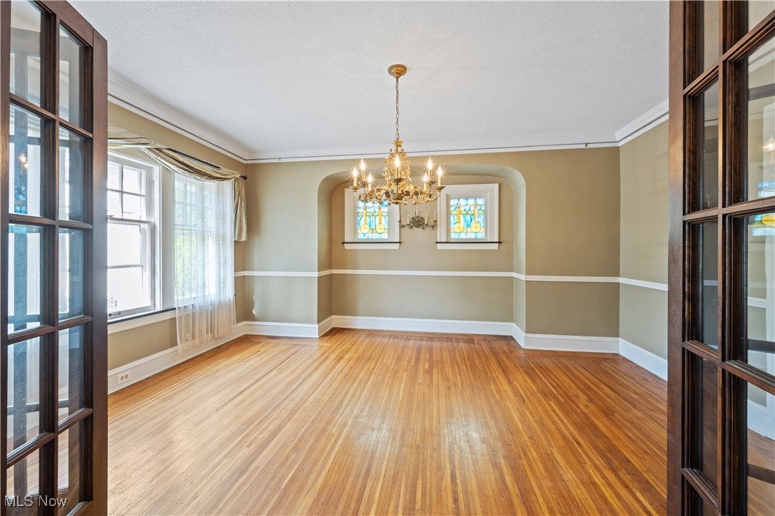 24510 Lake Road Bay Village, OH 44140 - Photo 15 of 45 Unfurnished dining area with arched walkways, plenty of natural light, wood finished floors, a chandelier, and ornamental molding