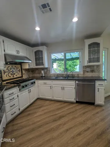 a large kitchen with granite countertop a stove top oven a sink a window and white cabinets