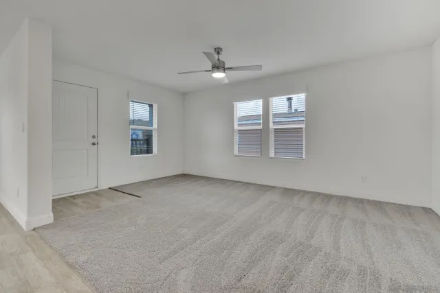 an empty room with a chandelier fan and windows
