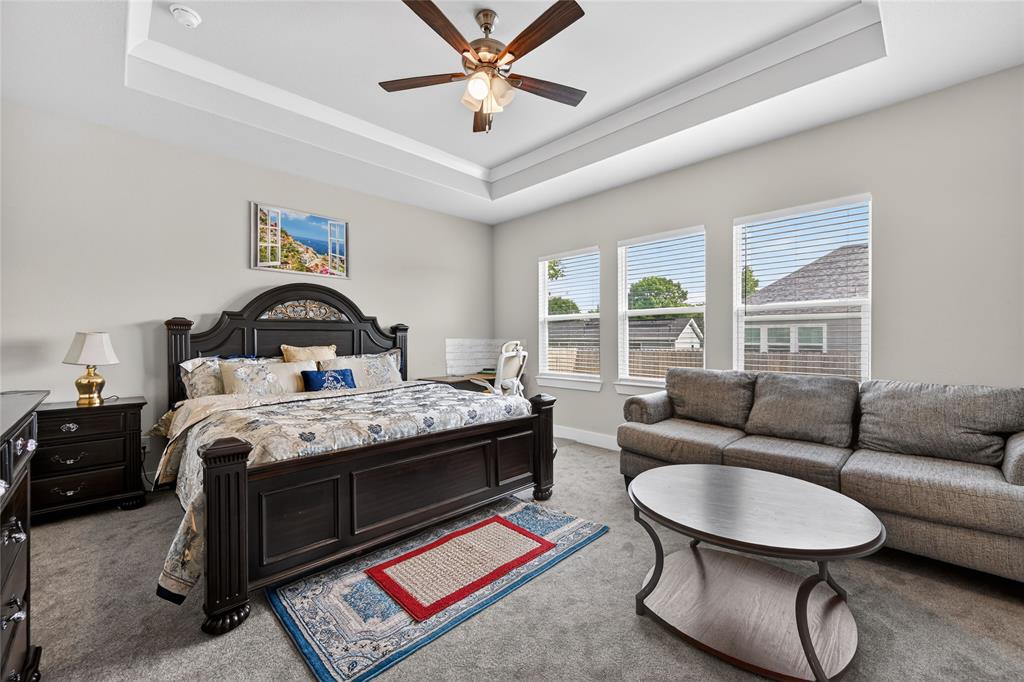 411 West Harwood Road Euless, TX 76039 - Photo 15 of 29 This spacious bedroom features a tray ceiling with a ceiling fan, plush grey carpeting, and three large windows providing natural light
