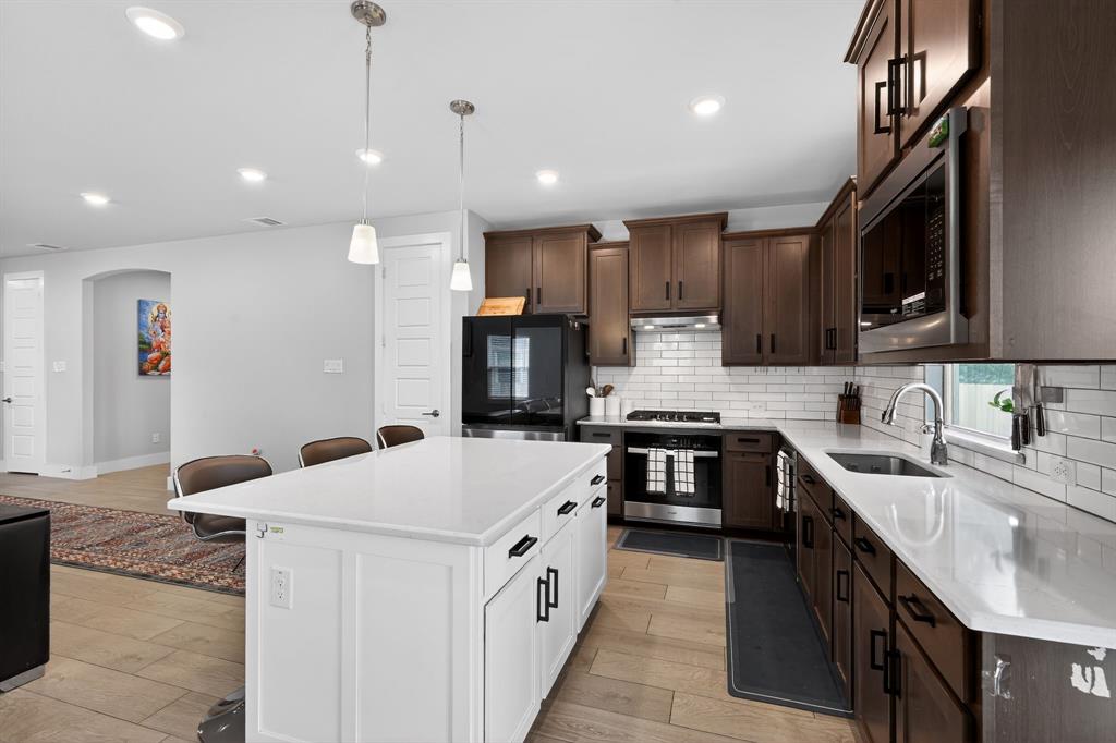 411 West Harwood Road Euless, TX 76039 - Photo 7 of 29 The kitchen features a white island with a countertop, dark wood cabinetry, stainless steel appliances, and a white subway tile backsplash
