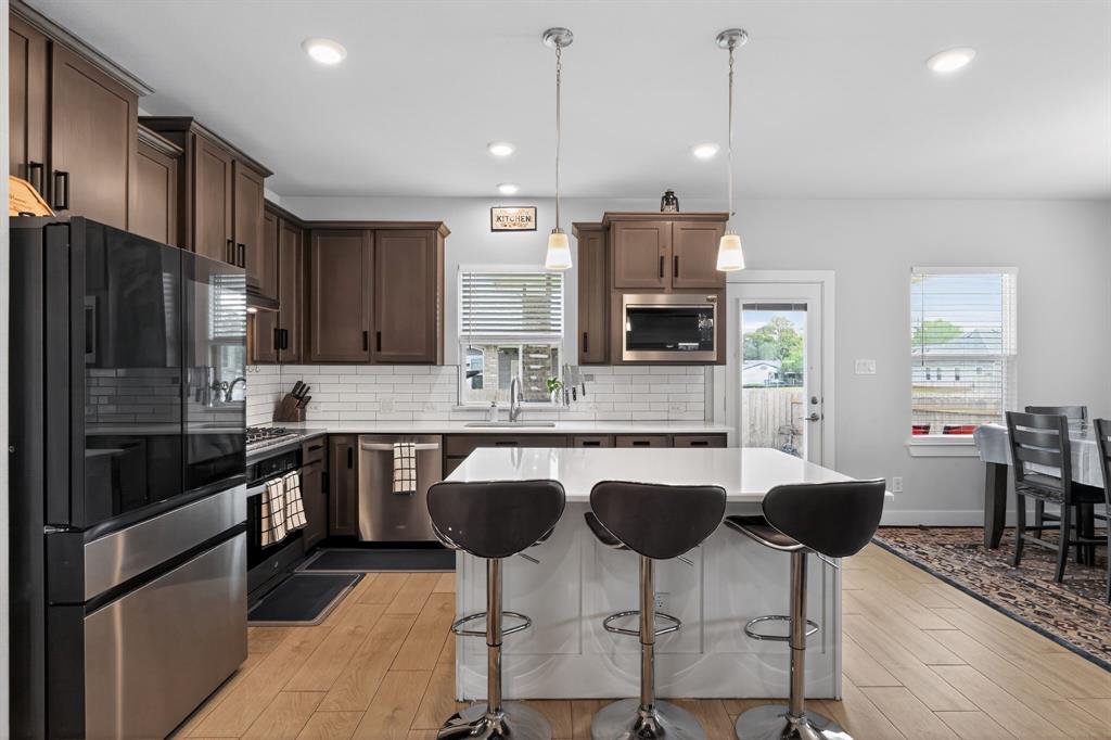 411 West Harwood Road Euless, TX 76039 - Photo 8 of 29 Kitchen featuring dark wood cabinetry, stainless steel appliances, a white subway tile backsplash, and a central island with pendant lighting