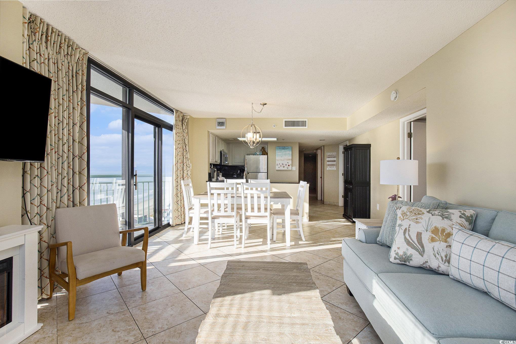 205 74th Avenue North, Unit 1810 Myrtle Beach, SC 29572 - Photo 20 of 37 Living room with light tile patterned floors, a chandelier, a water view, expansive windows, and a glass covered fireplace