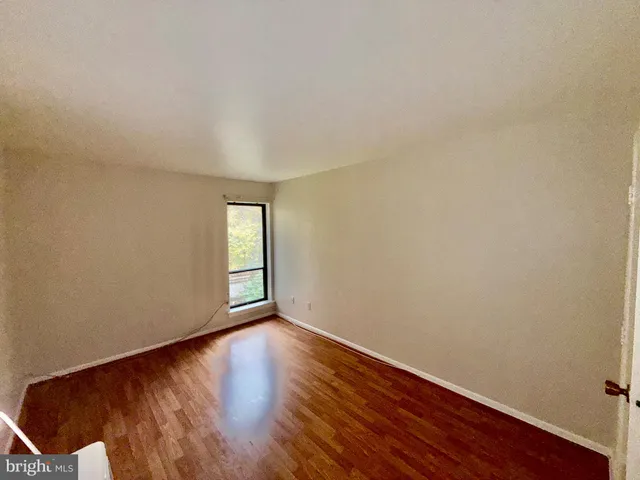 a view of an empty room with wooden floor and fan