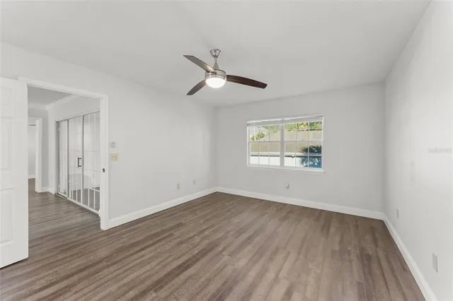 an empty room with wooden floor ceiling fan and windows