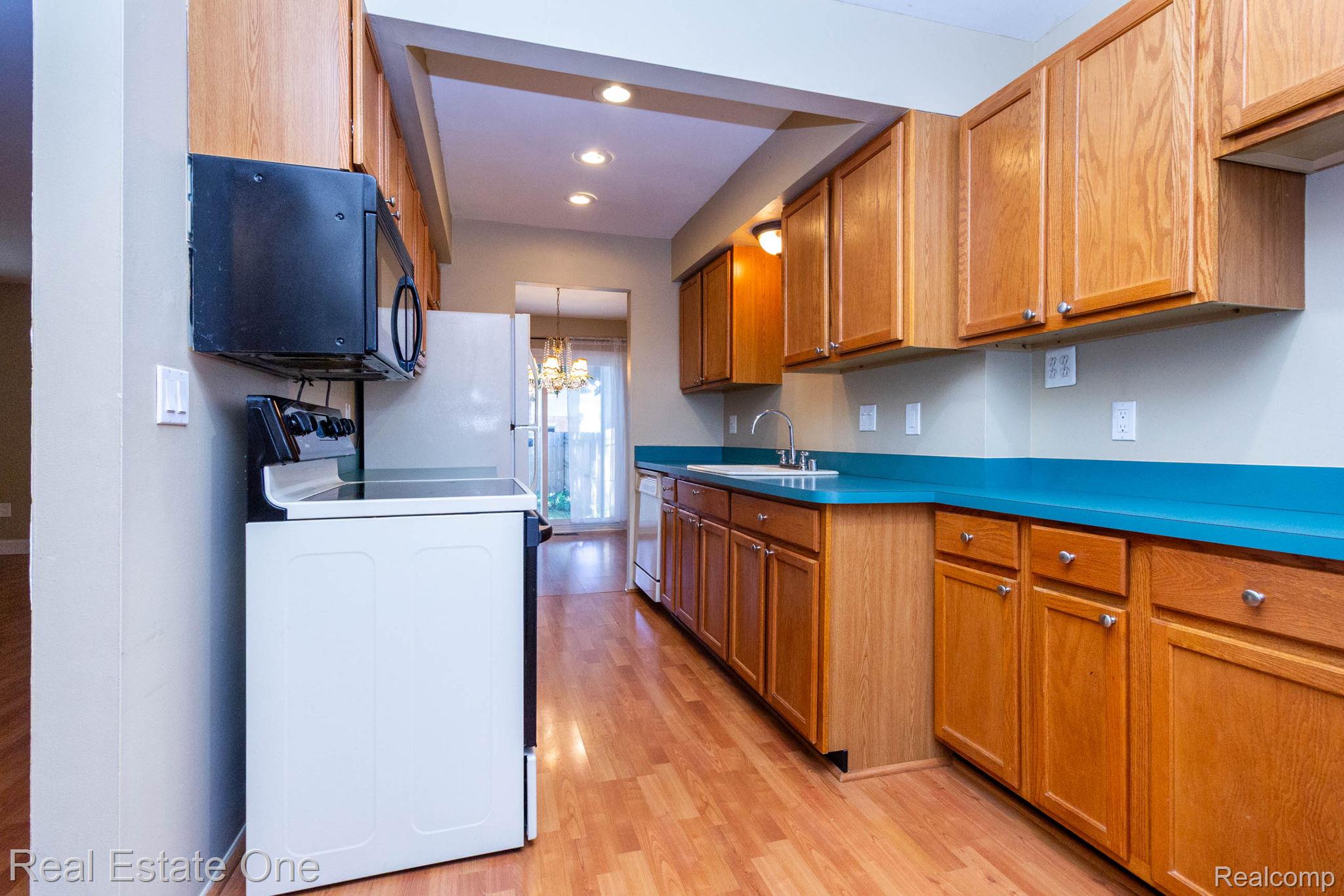 111 Manor Way Rochester, MI 48309 - Photo 11 of 36 Kitchen featuring abundant wood cabinetry, teal countertops, wood-finish flooring, a white range, and an over-the-range microwave