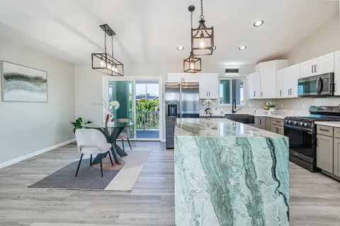 a kitchen with stainless steel appliances granite countertop a stove top oven a sink a dining table and chairs with wooden floor