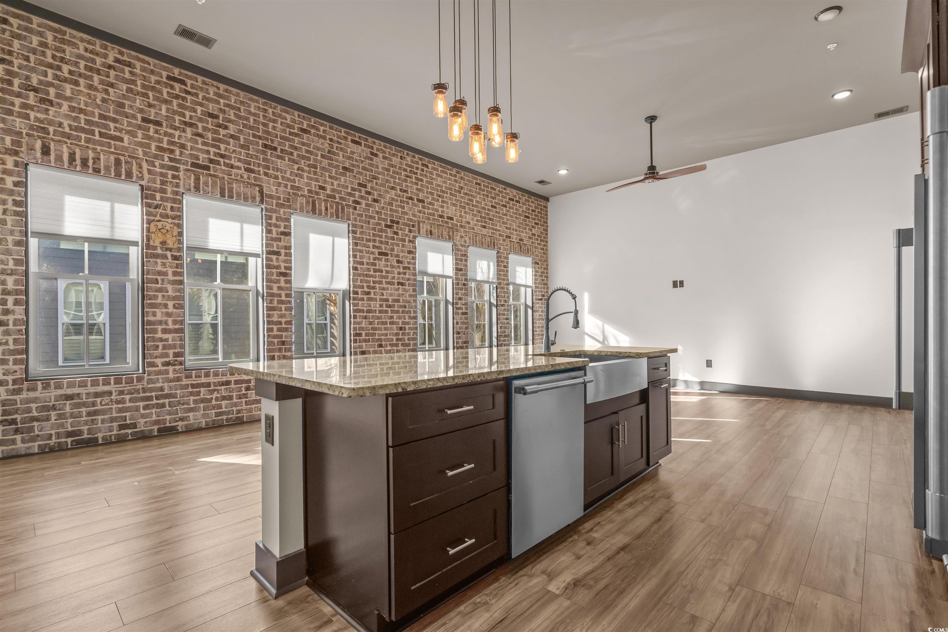 80 Shady Oak Lane Murrells Inlet, SC 29576 - Photo 9 of 31 Kitchen featuring brick wall, dark brown cabinetry, light stone counters, hanging light fixtures, and light wood-style floors