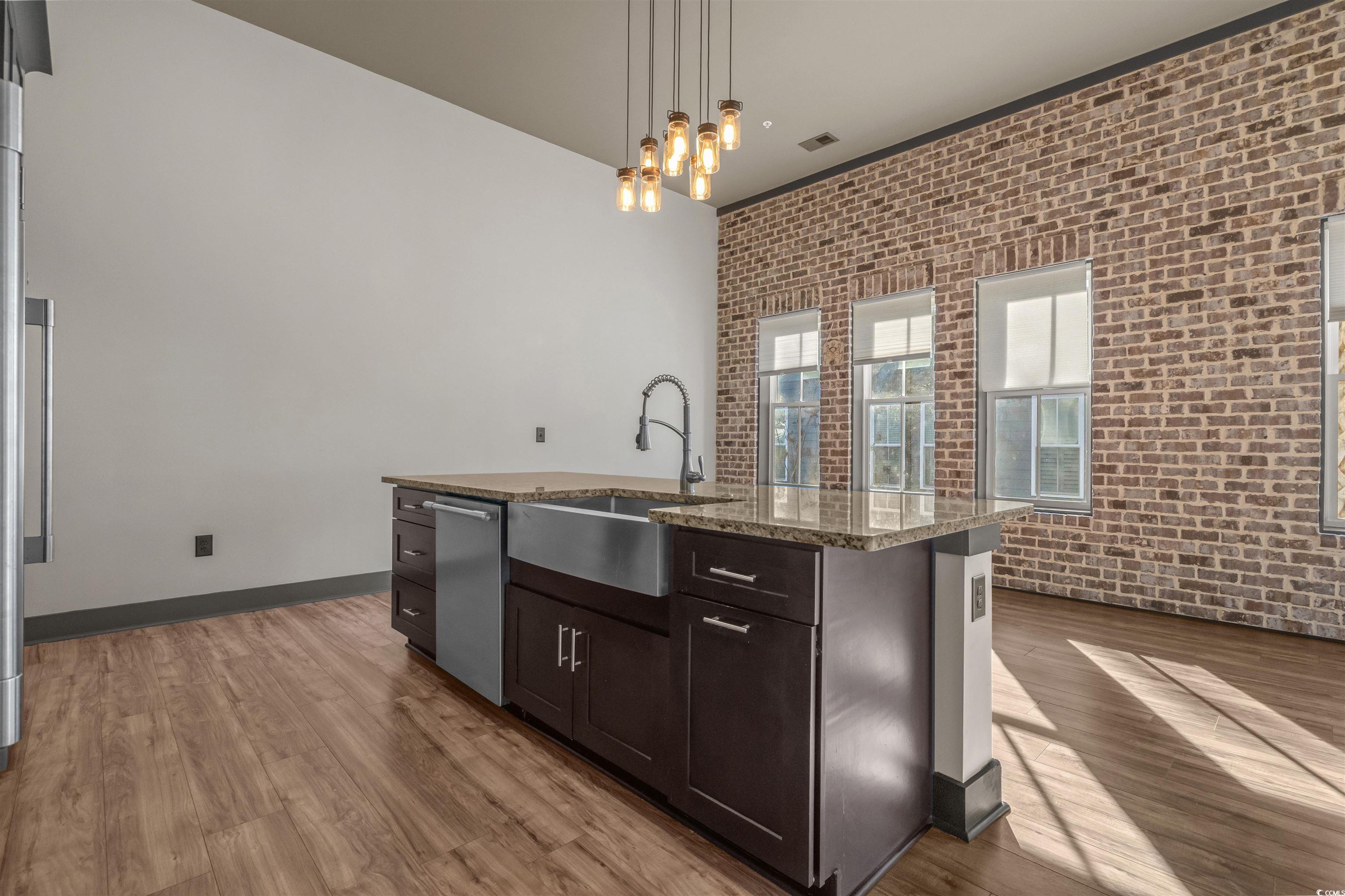 80 Shady Oak Lane Murrells Inlet, SC 29576 - Photo 10 of 31 Kitchen featuring brick wall, decorative light fixtures, dark brown cabinets, a center island with sink, and light stone countertops