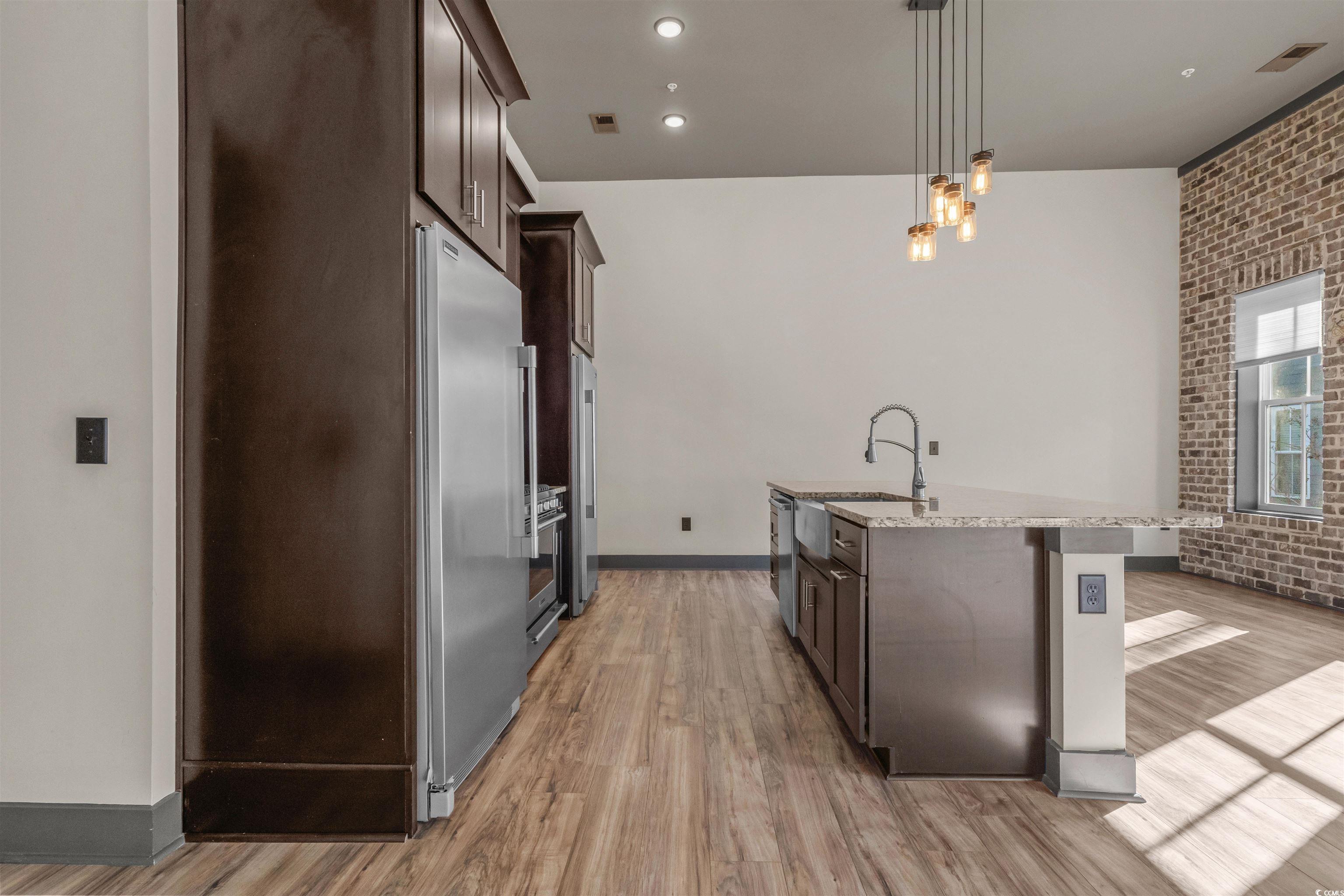 80 Shady Oak Lane Murrells Inlet, SC 29576 - Photo 11 of 31 Kitchen with brick wall, dark brown cabinetry, decorative light fixtures, stainless steel appliances, and light stone countertops