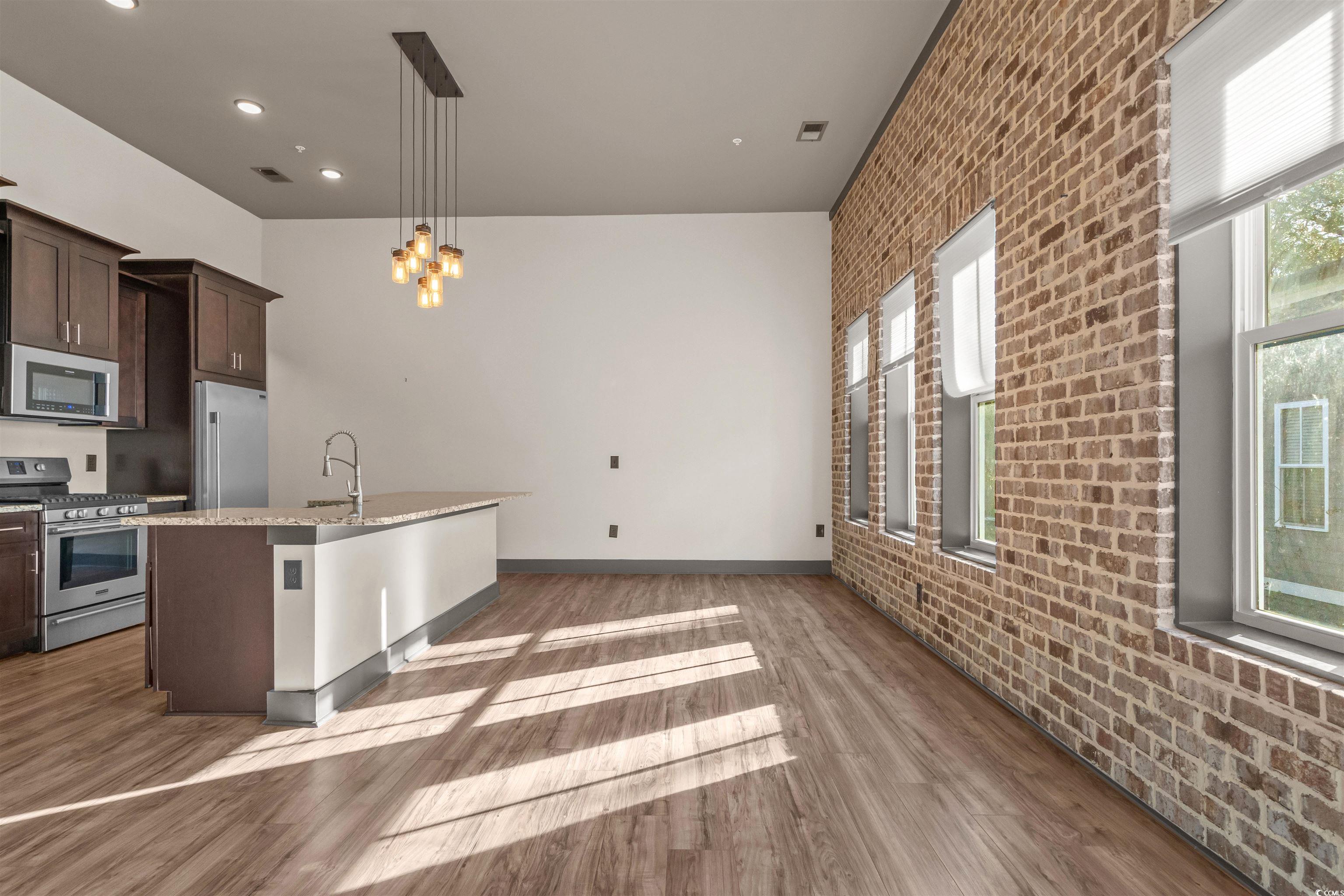 80 Shady Oak Lane Murrells Inlet, SC 29576 - Photo 7 of 31 Kitchen featuring brick wall, stainless steel appliances, dark brown cabinets, pendant lighting, and a kitchen island with sink