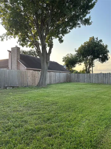 a view of a backyard with large trees and wooden fence