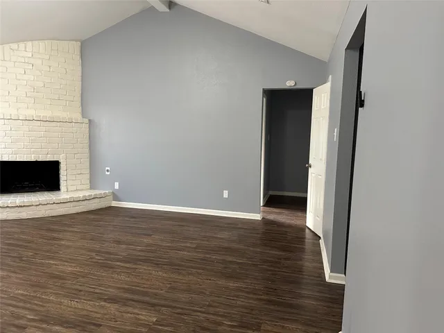a view of an empty room with wooden floor and a fireplace