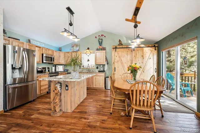 a kitchen with stainless steel appliances kitchen island granite countertop a refrigerator a stove a sink dishwasher and a dining table with wooden floor