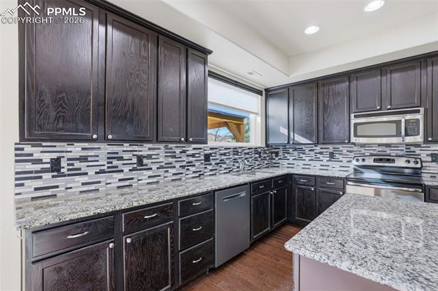 2224 Reed Grass Way Colorado Springs, CO 80915 - Photo 18 of 39 Kitchen with stainless steel appliances, light stone counters, dark wood-type flooring, dark brown cabinetry, and recessed lighting