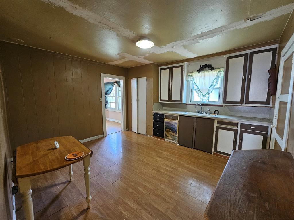 127 East Morgan Street Pilot Point, TX 76258 - Photo 16 of 25 Kitchen with light wood-style floors, light countertops, dishwashing machine, wood walls, and dark brown cabinetry