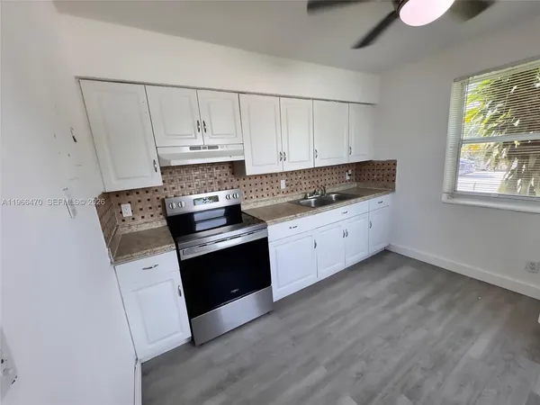 a kitchen with granite countertop a stove a sink dishwasher and white cabinets with wooden floor
