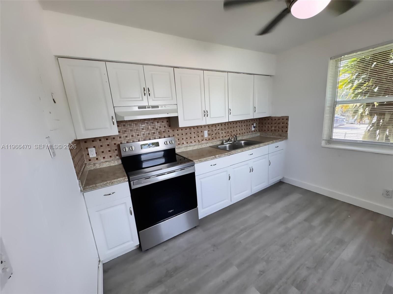 3450 Southwest 7th Street, Unit 3450 Miami, FL 33135 - Photo 7 of 7 a kitchen with granite countertop a stove a sink dishwasher and white cabinets with wooden floor
