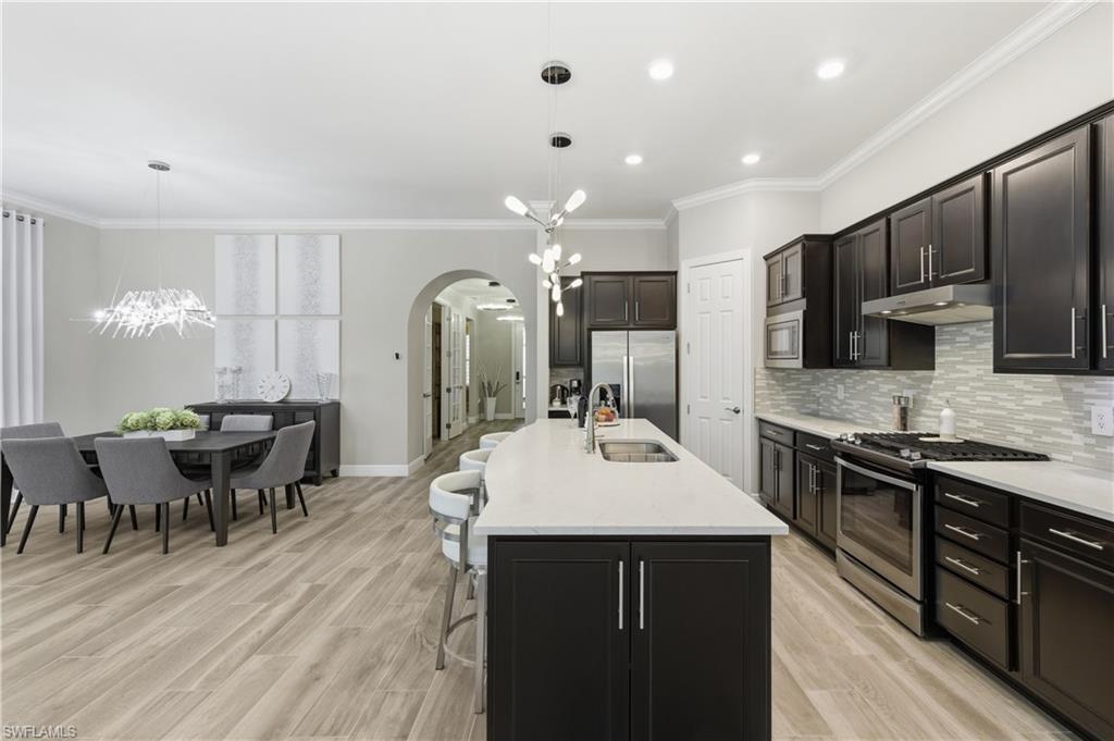 9761 Willet Court Naples, FL 34120 - Photo 18 of 44 a large kitchen with stainless steel appliances a stove center island a dining table and chairs