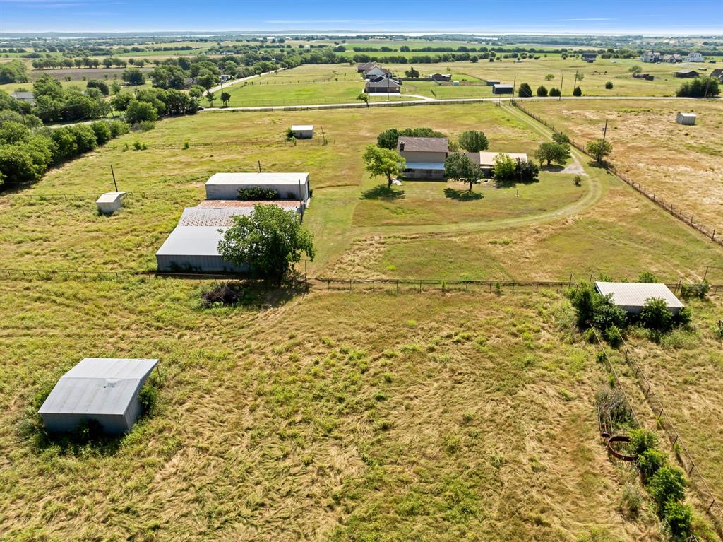 1795 Melton Road Sanger, TX 76266 - Photo 16 of 17 Expansive rural property featuring a primary residence with a covered porch, multiple outbuildings including a large barn with a metal roof, and a winding dirt driveway