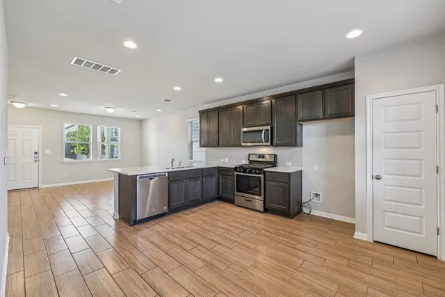 a kitchen with stainless steel appliances kitchen island granite countertop a stove a refrigerator a sink a oven with wooden cabinets and wooden floor