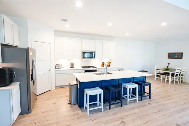 a kitchen with stainless steel appliances kitchen island a table chairs in it and white cabinets