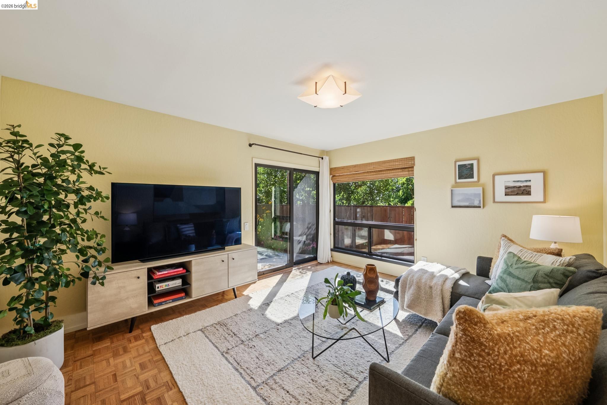 576 Vistamont Avenue Berkeley, CA 94708 - Photo 30 of 33 Living area featuring wood-finish parquet flooring, a sliding glass door, and a large window with a woven wood shade