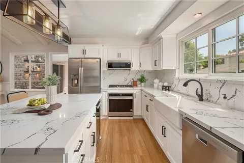 a kitchen with stainless steel appliances granite countertop a stove a sink dishwasher a refrigerator and white cabinets with wooden floor