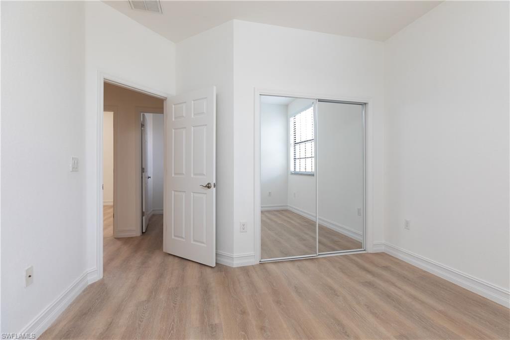 15618 Summit Pl Circle, Unit 396 Naples, FL 34119 - Photo 18 of 41 an empty room with wooden floor and mirror