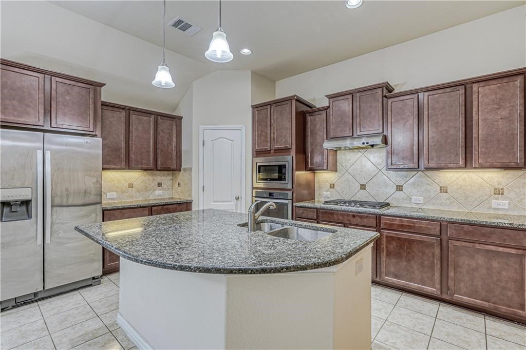 3517 Grail Hollows Road Pflugerville, TX 78660 - Photo 30 of 40 a kitchen with kitchen island granite countertop a sink stove and refrigerator