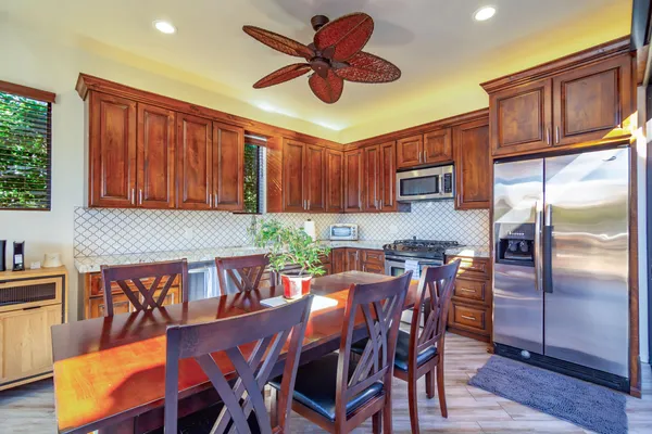 a kitchen with stainless steel appliances granite countertop a dining table chairs refrigerator and sink