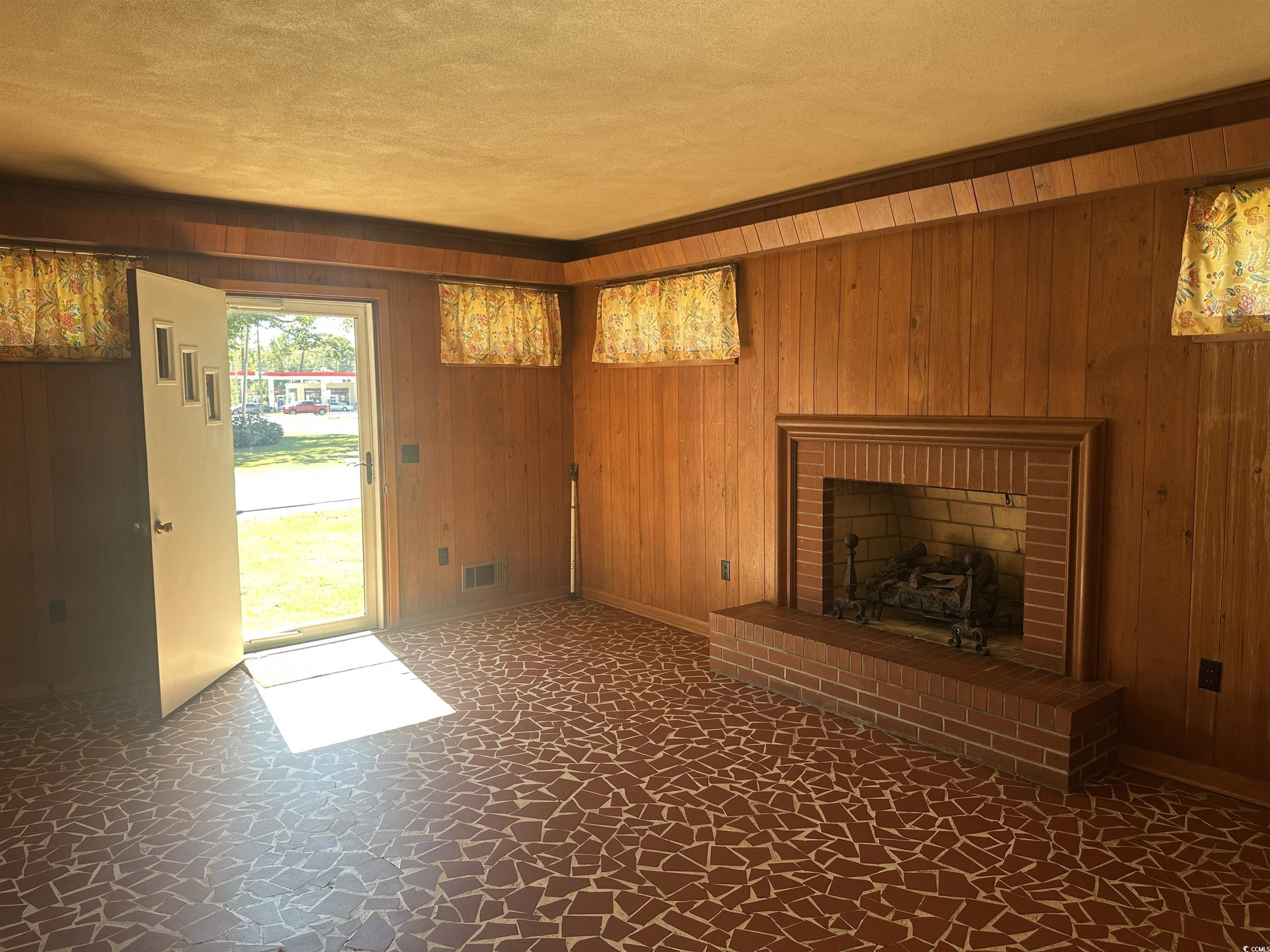 103 East 2nd Avenue Lake View, SC 29563 - Photo 8 of 16 Unfurnished living room with wooden walls, a brick fireplace, and a textured ceiling