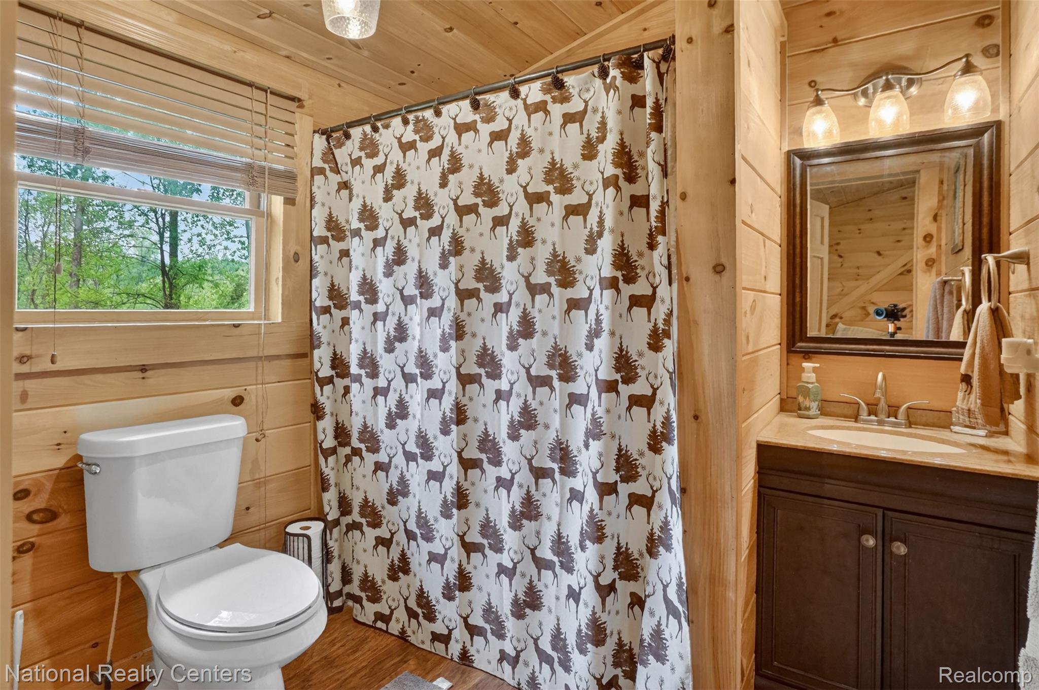 7782 Golf Club Road Howell, MI 48843 - Photo 20 of 27 Bathroom with wood-finish paneling, a single vanity with a light-toned countertop, and a window with horizontal blinds offering exterior scenery