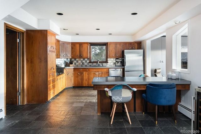 a kitchen with stainless steel appliances granite countertop a refrigerator a sink dishwasher a dining table and chairs with wooden floor