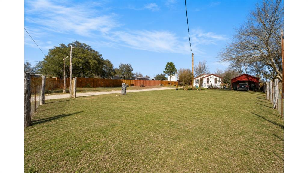 117 Reading Avenue North Center Point, TX 78010 - Photo 4 of 20 Expansive grass lawn with a gravel driveway, mature trees, and a wooden fence bordering the property