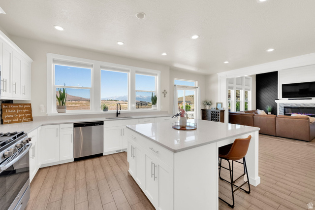 1857 Thunder Gulch Road Eagle Mountain, UT 84005 - Photo 12 of 50 Bright kitchen featuring white cabinetry, a large center island with seating, a stainless steel dishwasher, a gas range, and wood-finish flooring