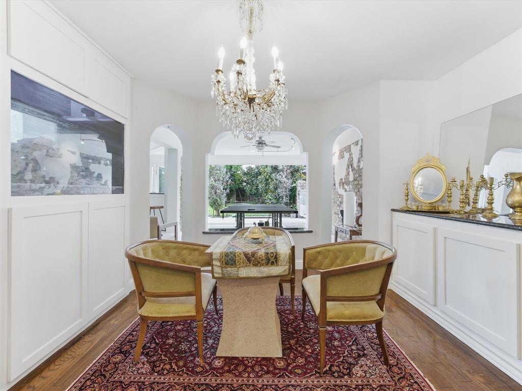 6160 Spring Valley Road Dallas, TX 75240 - Photo 15 of 40 Formal dining area featuring a crystal chandelier, arched doorways, a built-in aquarium, wood-finish flooring, and a large bay window overlooking outdoor landscaping