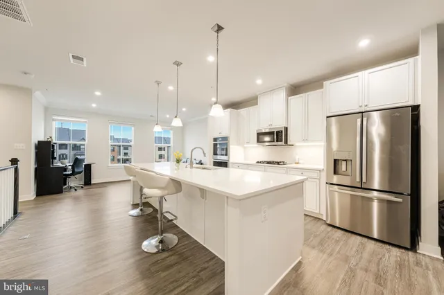 a kitchen with stainless steel appliances granite countertop a refrigerator a sink dishwasher a stove and white cabinets with wooden floor